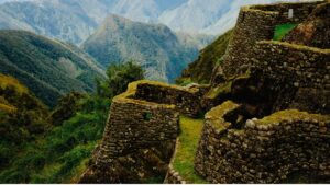 The moss-covered stone ruins and agricultural terraces of the Choquequirao archaeological site, perched high on a mountainside overlooking a deep Andean valley – Qosqo Expeditions