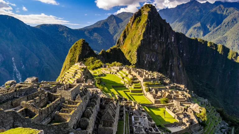 A stunning panoramic view of the ancient Inca citadel of Machu Picchu, with its intricate stone ruins and green terraces set against the Andes mountains. – Qosqo Expeditions