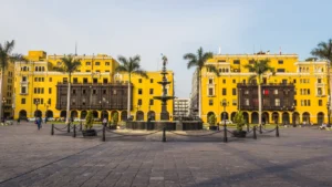 The sunny Plaza Mayor in Lima, Peru, featuring its central bronze fountain and iconic yellow colonial buildings with enclosed wooden balconies. – Qosqo Expeditions