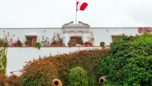 The beautiful white colonial facade of the Larco Museum in Lima, surrounded by vibrant flowering gardens, with the Peruvian flag flying above. – Qosqo Expeditions