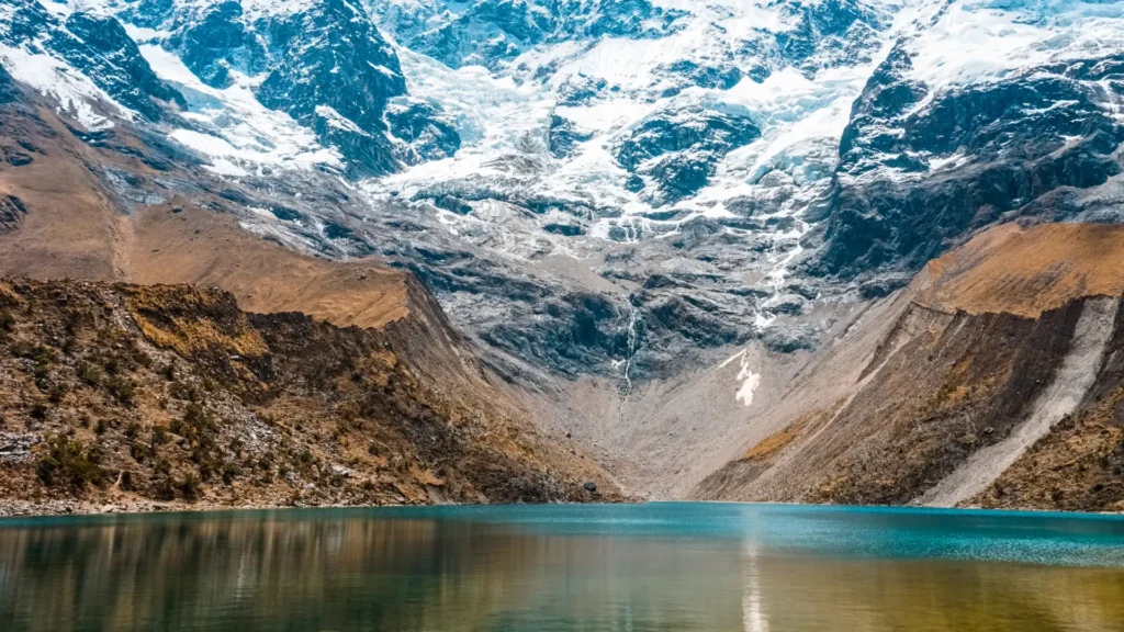 A close view of the tranquil, turquoise waters of Humantay Lake, with the massive, snow-covered Humantay glacier rising directly from its shore. – Qosqo Expeditions