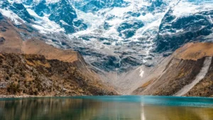 A close view of the tranquil, turquoise waters of Humantay Lake, with the massive, snow-covered Humantay glacier rising directly from its shore. – Qosqo Expeditions