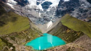 A high-angle view of the brilliant turquoise Humantay Lake, nestled at the base of the immense, snow-covered Humantay glacier in the Peruvian Andes. – Qosqo Expeditions