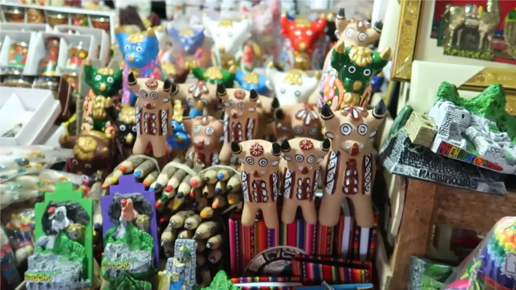 A display of colorful Peruvian handicrafts and souvenirs, including Ekeko figurines and miniature Machu Picchu replicas, representing unique Cusco experiences and local artistry. - Qosqo Expeditions
