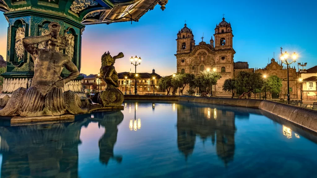 The beautiful main square of Cusco, Peru, at dusk, featuring the illuminated fountain and the cathedral, highlighting memorable Cusco experiences. - Qosqo Expeditions
