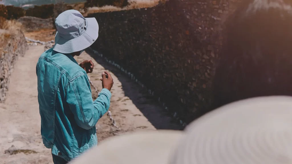 A traveler wearing a blue denim jacket and a bucket hat walking alongside an ancient Inca stone wall bathed in sunlight, a moment of discovery in bespoke Peru travel. - Qosqo Expeditions