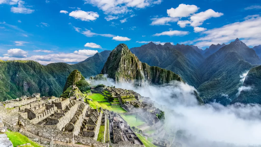 A breathtaking panoramic view of the ancient Inca citadel of Machu Picchu shrouded in clouds, nestled amidst towering green mountains, a highlight of any luxury Amazon Andes expedition. - Qosqo Expeditions