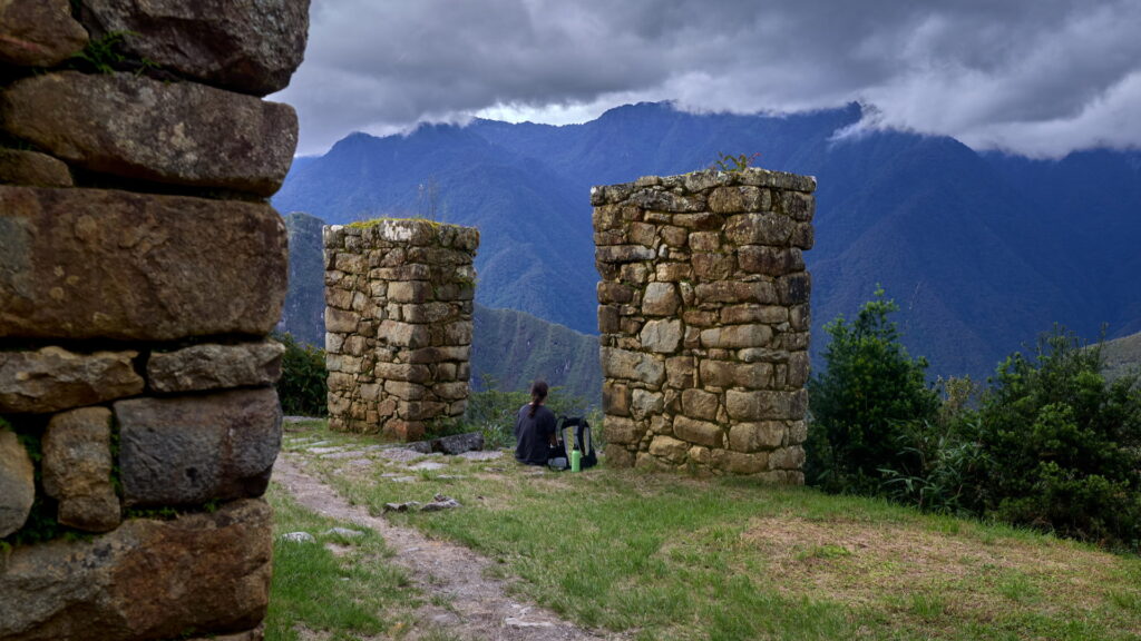 A person resting amidst ancient Inca stone structures with majestic mountains in the misty background, a peaceful moment on private Machu Picchu tours. - Qosqo Expeditions