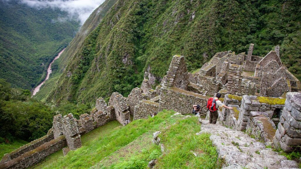 Hikers with backpacks exploring the ancient stone terraces of the Wiñay Wayna archaeological site, perched on a steep mountainside overlooking the Urubamba River valley on the Short Inca Trail to Machu Picchu – Qosqo Expeditions
