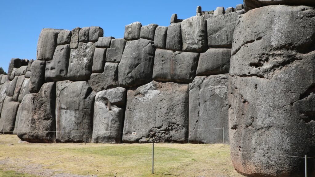 A close-up view of the massive megalithic stone walls of the Inca fortress Sacsayhuaman in Cusco, showing the precise fitting of the giant polygonal stones under a clear blue sky – Qosqo Expeditions