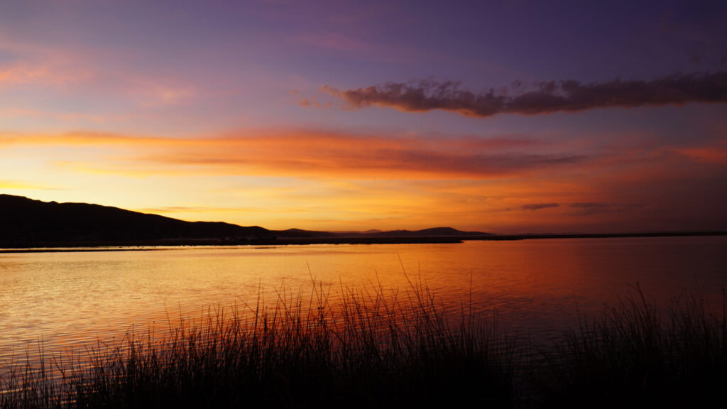 A serene sunset over Lake Titicaca, the mythical birthplace of the Incas, with golden and purple skies reflected in the water, a key location in any Inca mythology guide – Qosqo Expeditions