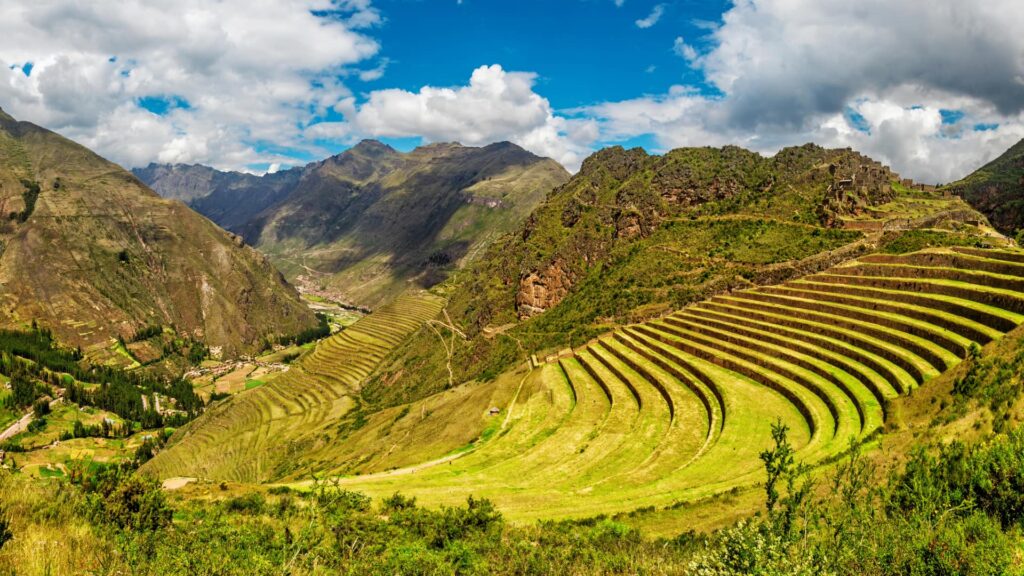 A wide, panoramic view of the ancient, curved Inca agricultural terraces at the Pisac archaeological site, set against the vast mountains of the Sacred Valley, a perfect setting for a Sacred Valley wellness retreat – Qosqo Expeditions