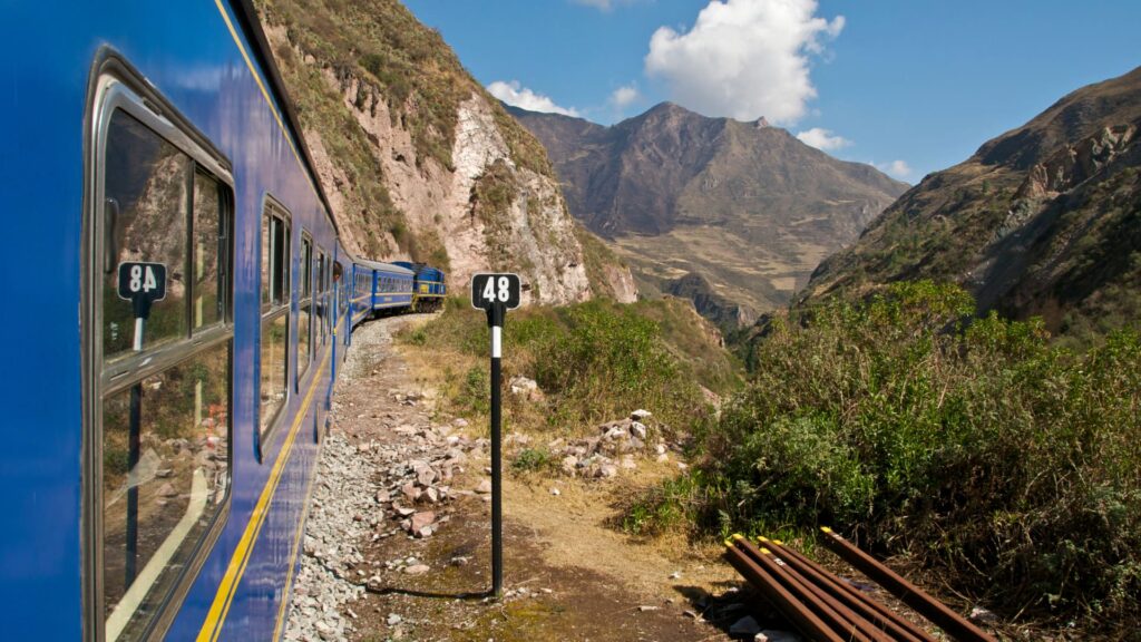 The blue PeruRail or Inca Rail train traveling through the scenic Urubamba River valley on its way to KM 104, the starting point of the Short Inca Trail to Machu Picchu – Qosqo Expeditions