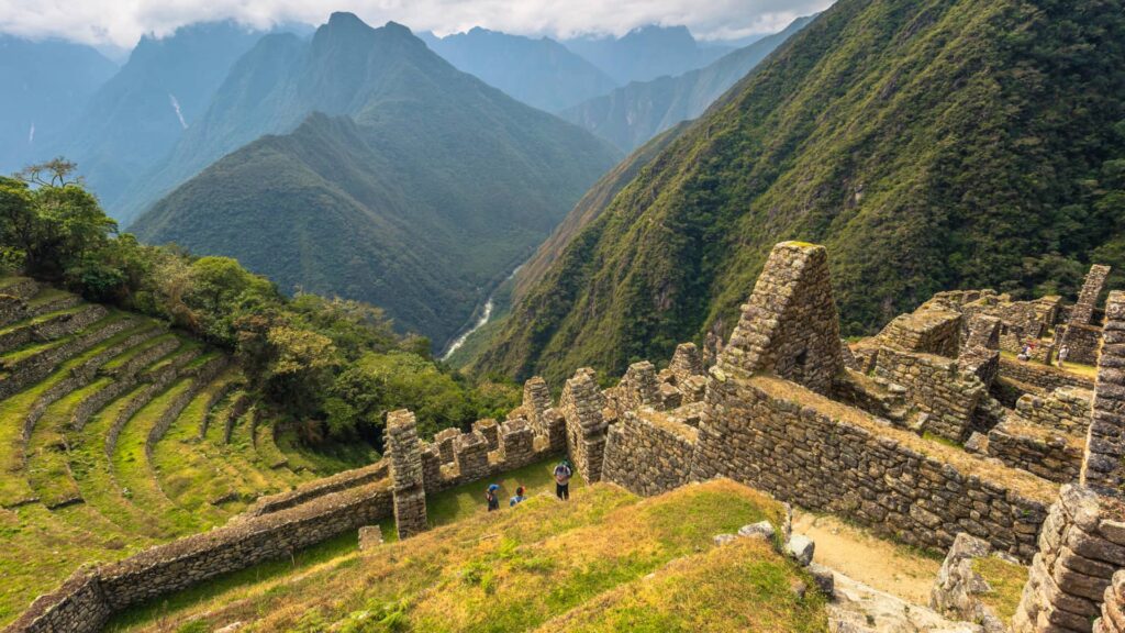 View from the Wiñay Wayna ruins on the Inca Trail, showing the stone structures and agricultural terraces overlooking the vast Urubamba River valley and Andean mountains – Qosqo Expeditions