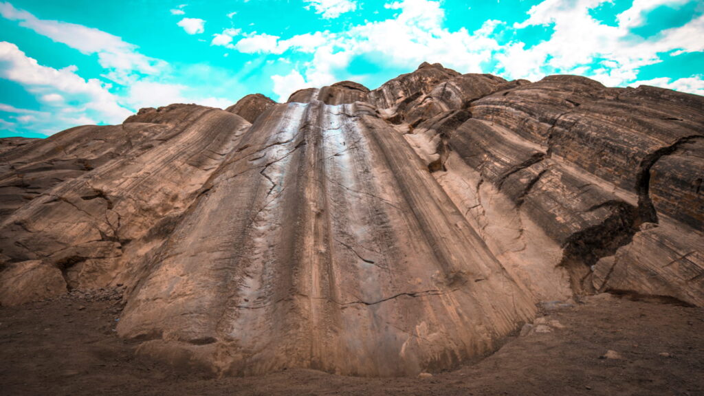 A low-angle view of the large, smooth Rodadero rock slides at Sacsayhuaman, showing the natural glacial polish and grooves under a bright blue sky – Qosqo Expeditions