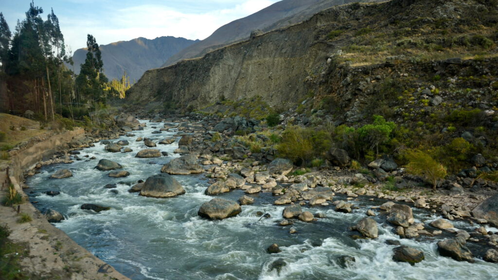 The powerful Urubamba River with its white water rapids flowing over large rocks, set in a deep Andean canyon in the Sacred Valley, an ideal scene for a Sacred Valley wellness retreat walk – Qosqo Expeditions