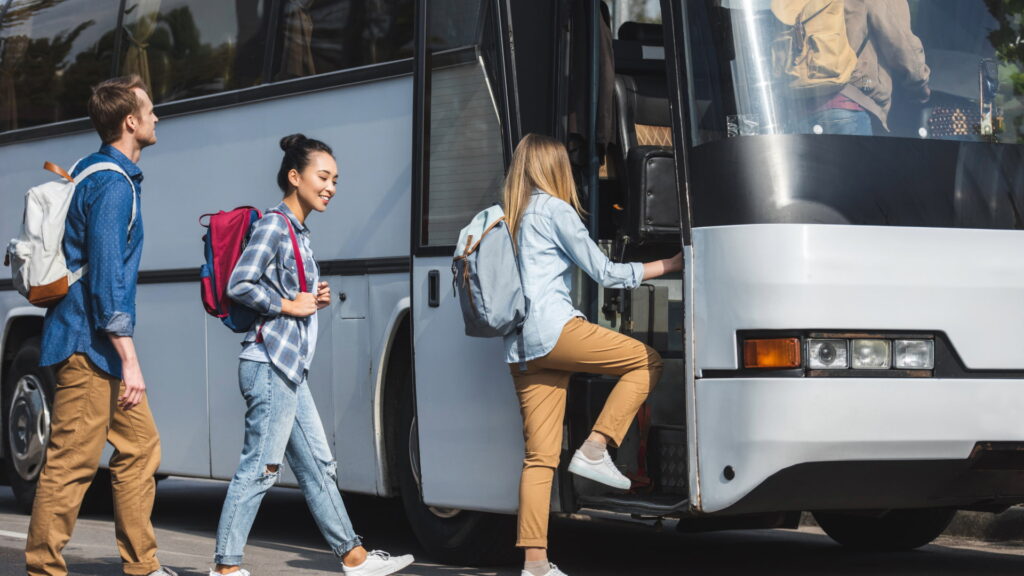 A group of young travelers with backpacks smiling as they board a modern tour bus for a long-distance journey in Peru – Qosqo Expeditions