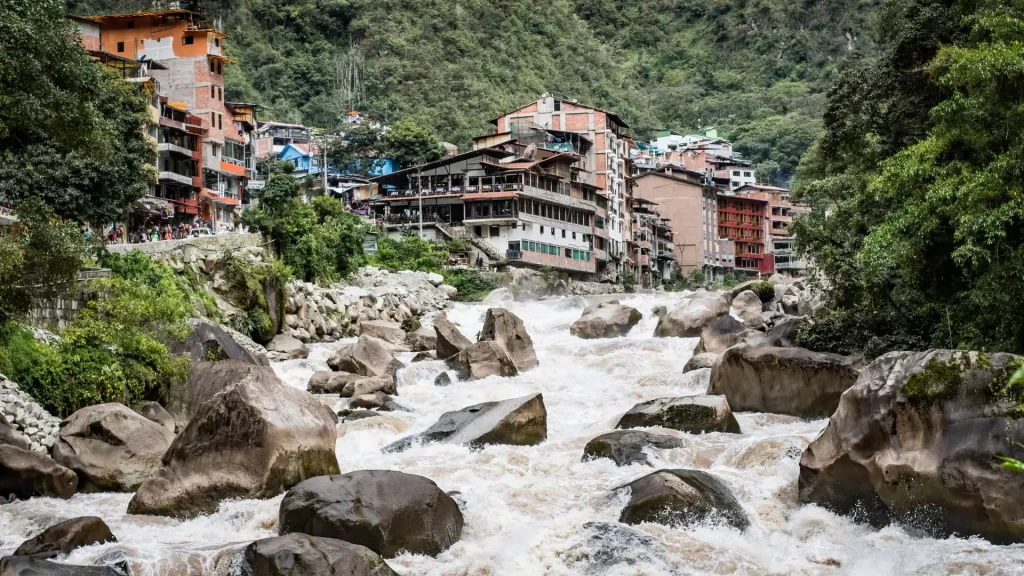View of Aguas Calientes town built along a rushing river, surrounded by steep green hills—an essential stop on the Machu Picchu express tour.-Qosqo Expeditions