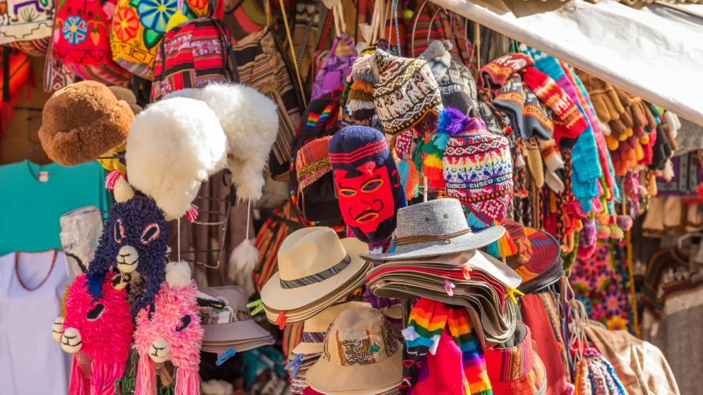 Colorful market stall in Cusco displaying traditional Andean hats knitted balaclavas plush alpaca toys and handmade gloves-Qosqo Expeditions