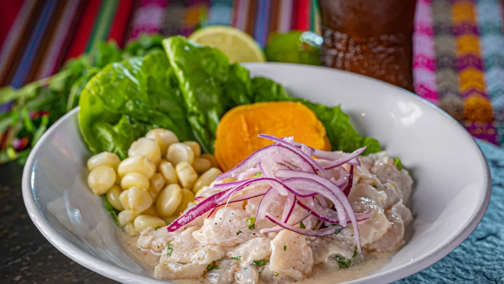 Traditional Peruvian ceviche with red onion, choclo, sweet potato, and chicha morada on a colorful Andean textile-Qosqo Expeditions