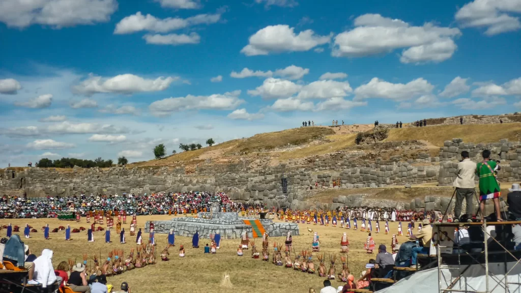 Traditional Andean performers at Sacsayhuamán during Inti Raymi, with stone ruins and spectators featured in the Inti Raymi festival guide.-Qosqo Expeditions