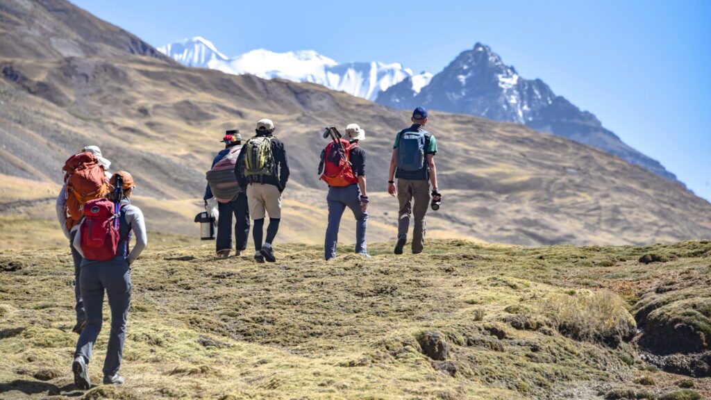 A group of hikers trekking through the high Andes mountains under a clear blue sky, with snow-capped peaks in the distance and local guides carrying traditional gear.-Qosqo Expeditions