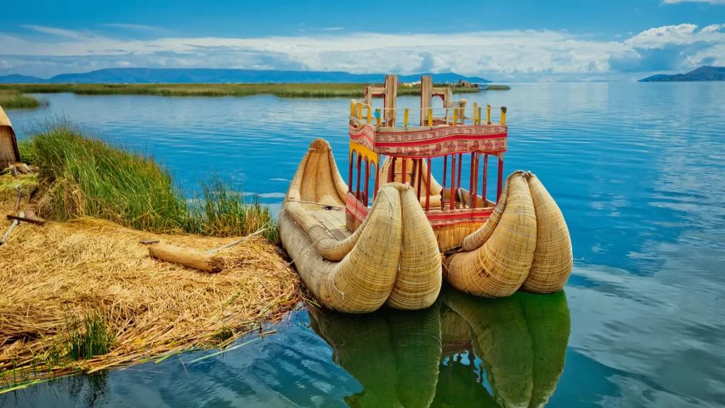 Traditional reed boat floating on Lake Titicaca near Puno, with mountains and sky in the background-Qosqo Expeditions