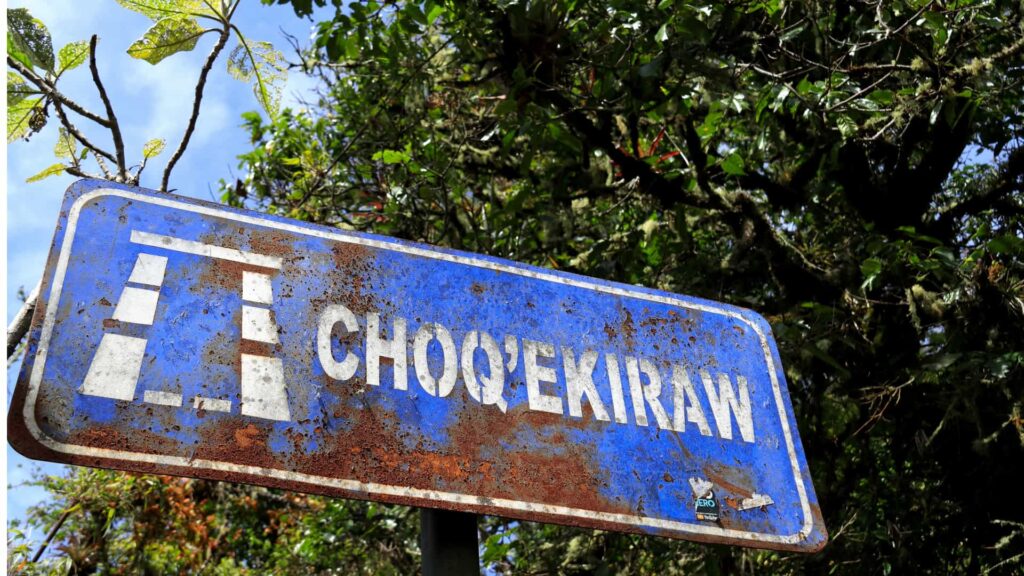 Weathered blue sign reading “CHOQEKIRAW” with stylized ruins, surrounded by forest—marking the Choquequirao trek Peru route.-Qosqo Expeditions