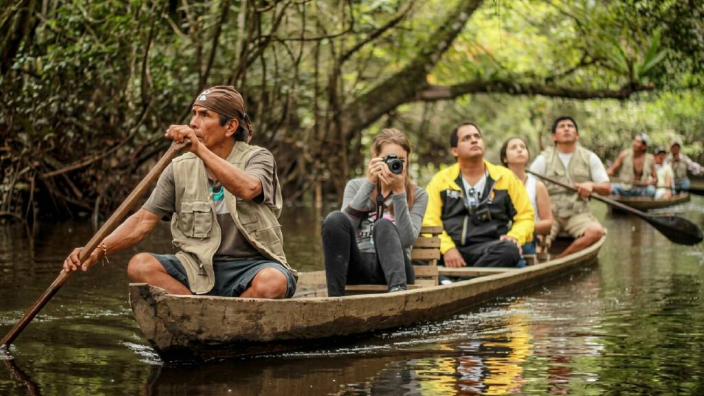 Tourists paddle a wooden canoe alongside a local guide down a river in the Amazon an ideal experience for tailor made holidays in Peru.