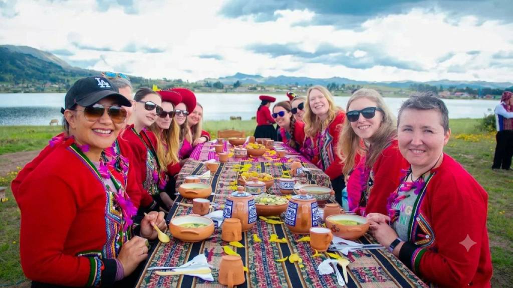 Tourists share a traditional lunch served on clay dishes by a lagoon during an experiential tourism activity in Cusco.