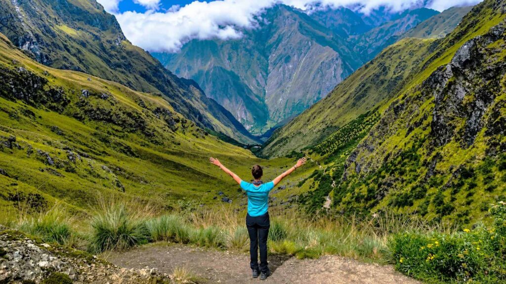A tourist with arms outstretched at Warmiwañusca Pass, the highest point on the Inca Trail at 4,215 meters above sea level.