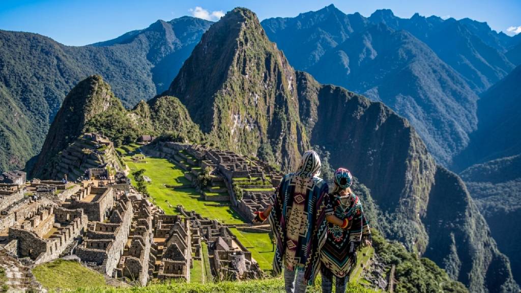 A couple wearing traditional Andean ponchos admiring Machu Picchu and Huayna Picchu Mountain during a tailor made holidays in Peru.