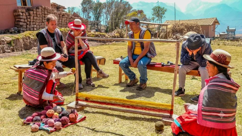 Foreign tourists learn traditional Andean weaving techniques alongside local artisans during an experiential tourism activity in Cusco.