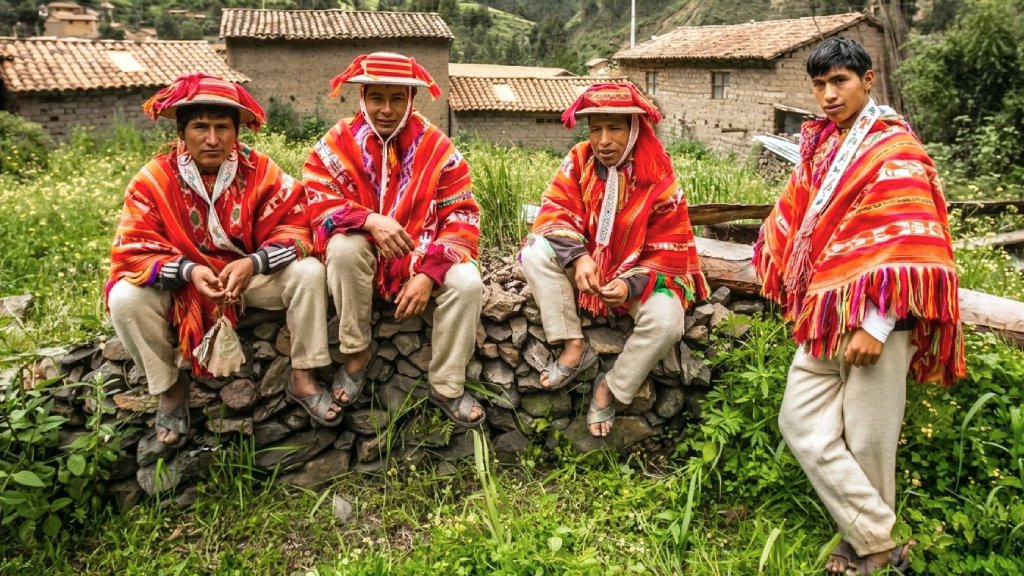Four men from the Huilloc Community wearing traditional ponchos near adobe houses in Cusco.
