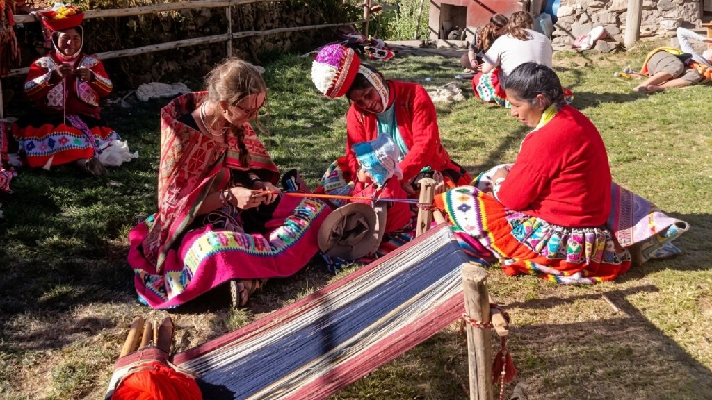 Tourist learning traditional weaving techniques with local women in the Huilloc Community.
