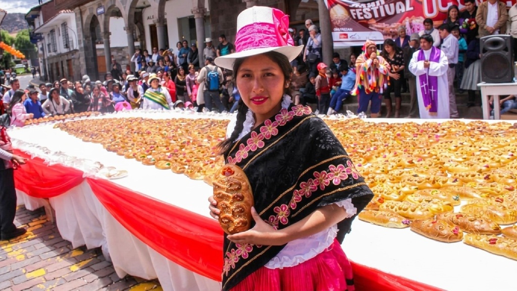 Woman wearing traditional Cusqueña clothing and holding a Tanta Wawa bread at a fair during the Day of the Dead in Peru.