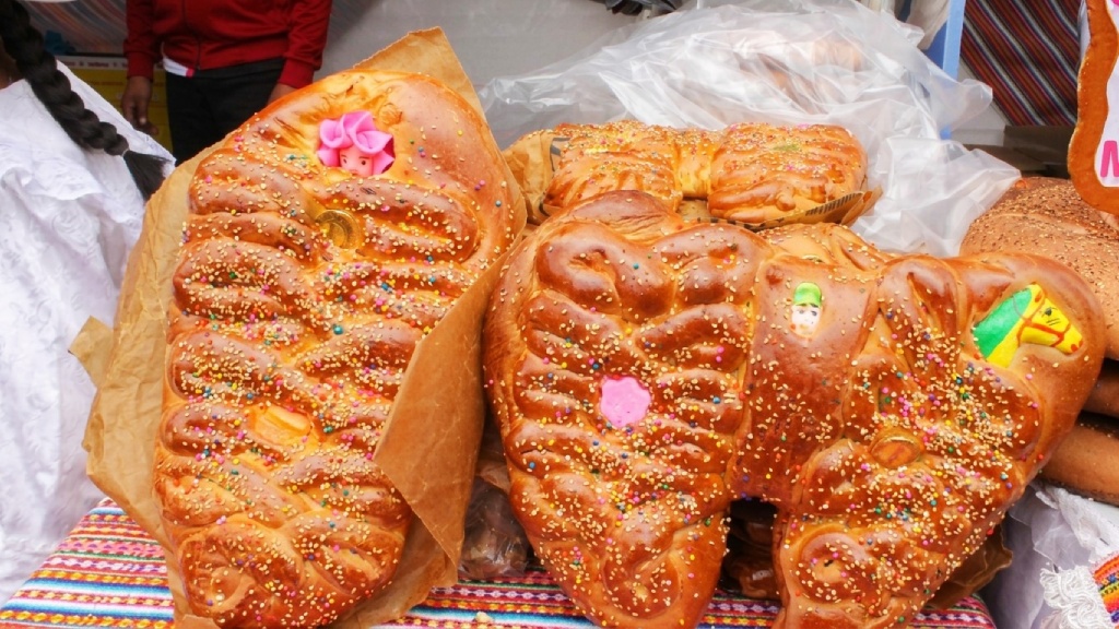 Traditional Tanta Wawa and Pan Caballo breads decorated with sesame seeds, colorful sprinkles, and small face-shaped figures for the Day of the Dead in Peru.