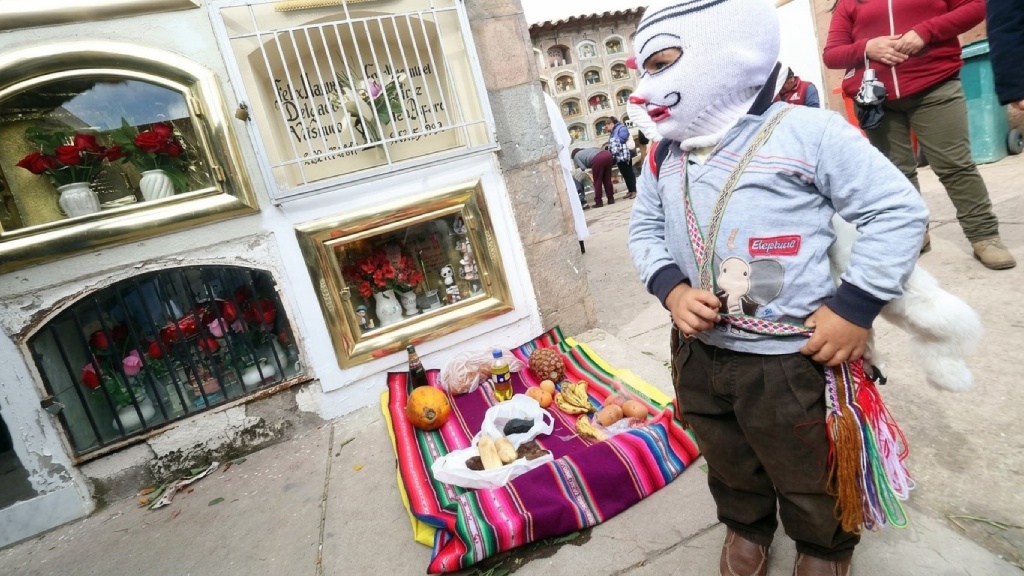 Traditional food and fruit offering arranged on a colorful Andean textile in a cemetery during the Day of the Dead in Peru.