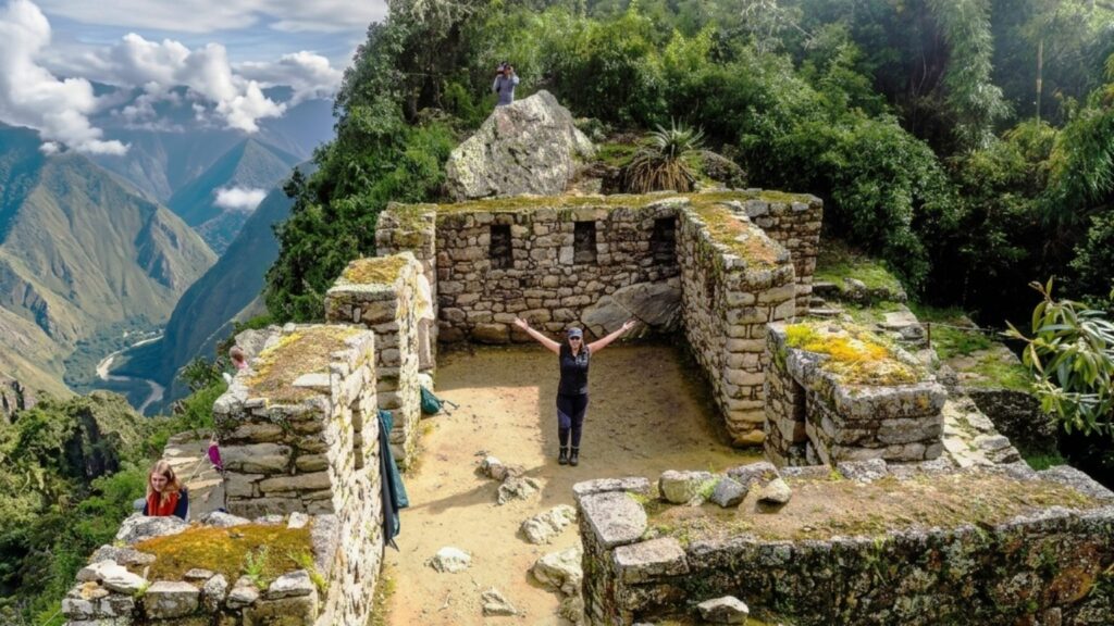 Hiker with arms outstretched beside the stone walls of Intipunku, also known as the Sun Gate.